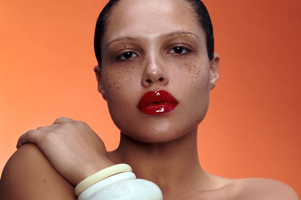 Portrait of model with red lipstick and white bangles against orange background