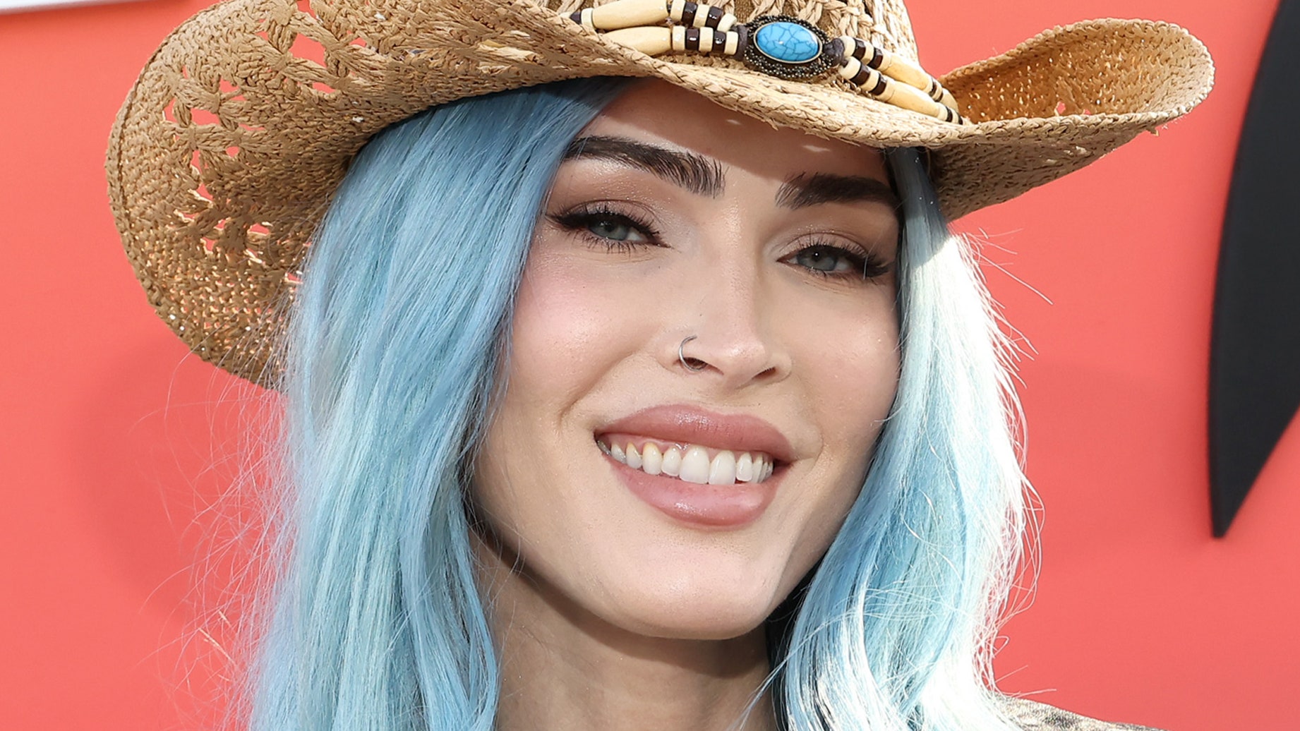 Megan Fox appears at an event with long blue hair and a cowboy hat.