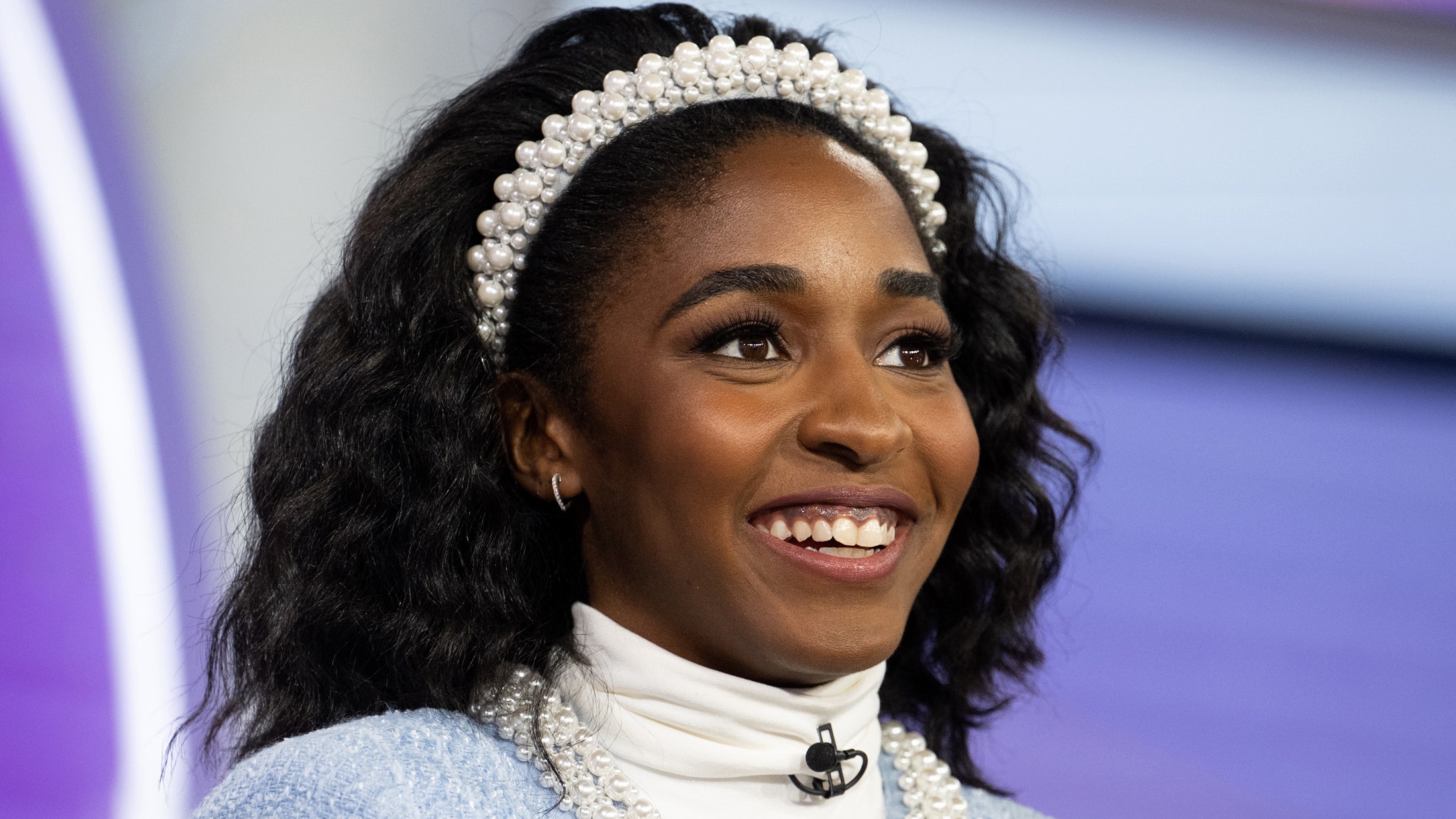 Ayo Edebiri appears at an event in a blue jacket and curls with a pearl headband.