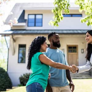 A couple meeting with real estate agent in front of home