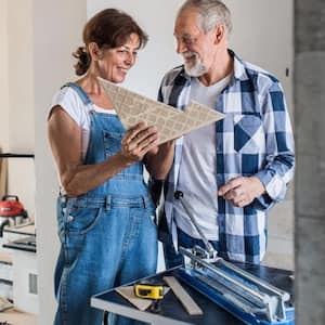 Senior couple laying tile floor in new home