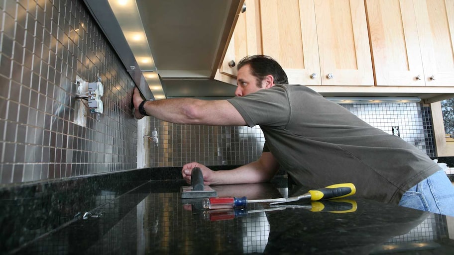 man installing metal backsplash in kitchen