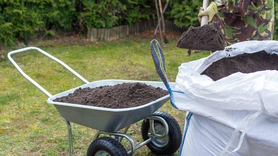 person pouring soil into wheelbarrow 