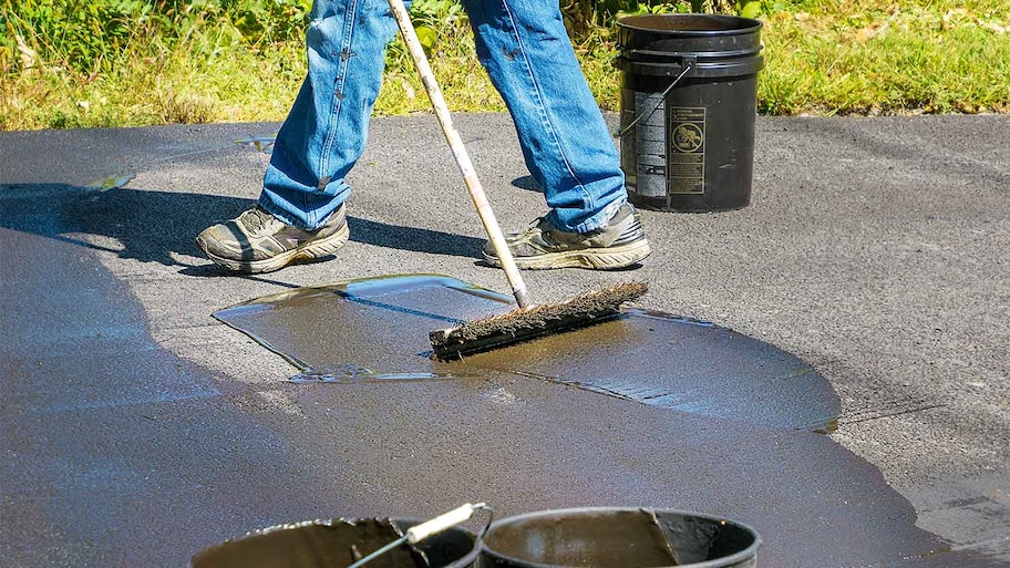 Worker using a brush to apply sealant on the driveway