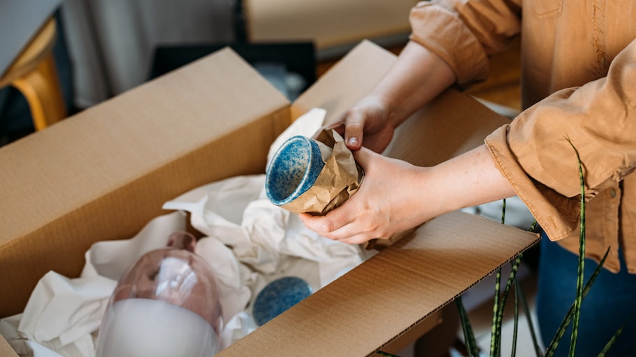 close up shot of hands of an anonymous person wrapping up fragile ceramic mug in packing paper