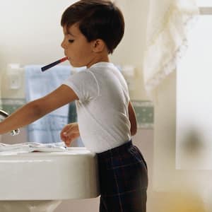 Boy with toothbrush in mouth turning off the tap