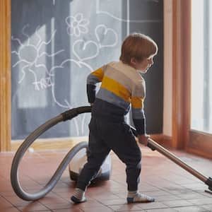 A boy with a vacuum in a room with ceramic tiles for flooring