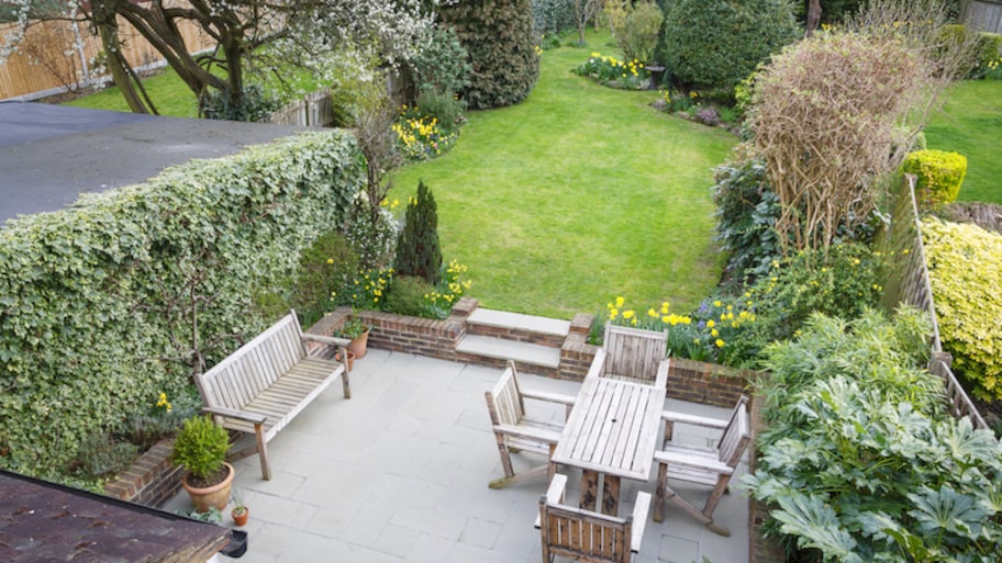 overhead view of concrete patio with lawn furniture next to lush garden flowers and plants and grassy yard