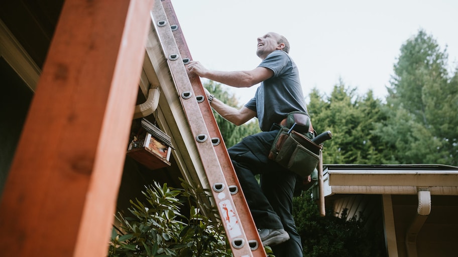 A contractor on a ladder checking a house’s roof