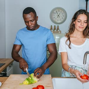 Couple rinses vegetables and prepares salad in kitchen