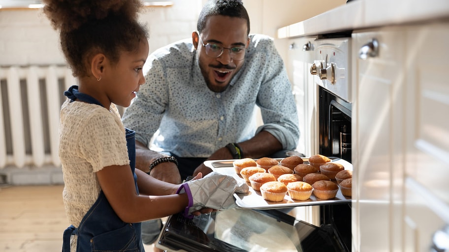 Dad watches daughter pulled baked muffins from oven