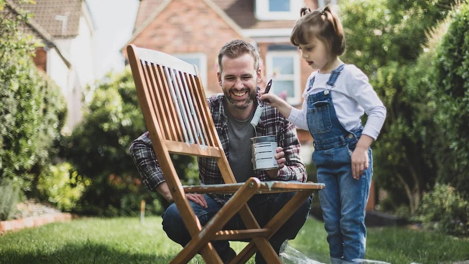 Father and daughter painting chair outside