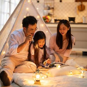 A family reading a book in front of a teepee tent