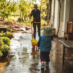 Young woman sweeping water from front yard on rainy day 