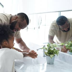 father helping his young daughter was her hands in sink with marble countertop