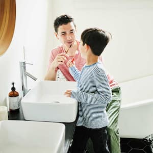 Father showing son how to brush his teeth in the bathroom