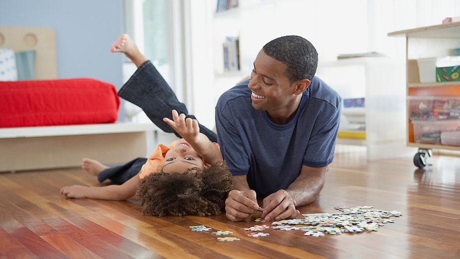 Father and daughter put together a puzzle on hardwood floors