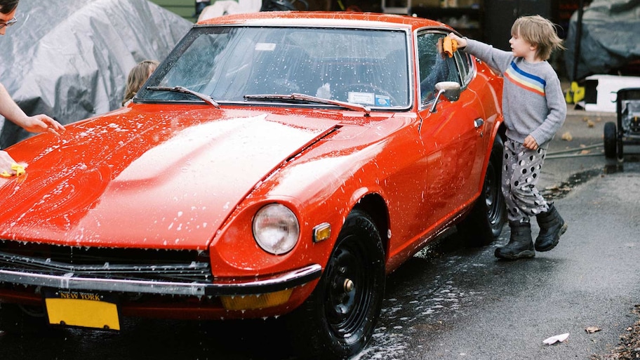 A little boy with his father wash their red vintage car in the driveway of their home