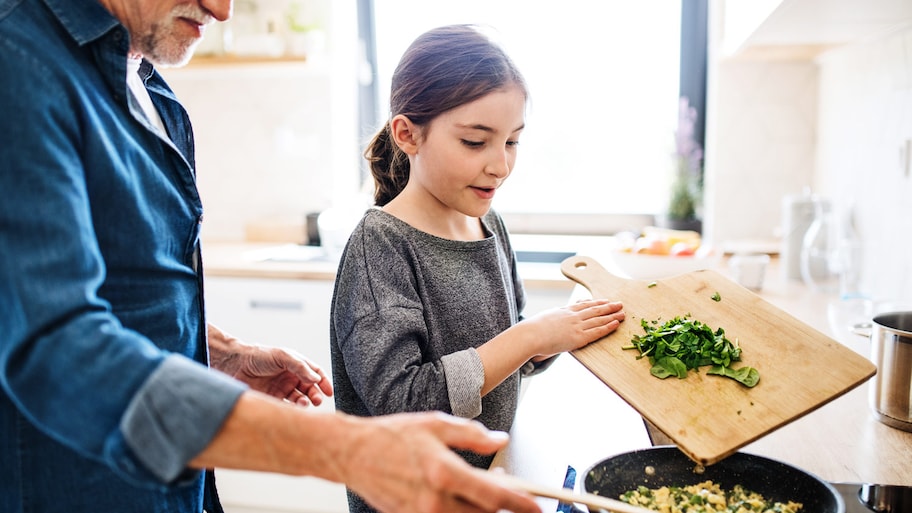 Senior grandfather and granddaughter preparing food indoors in kitchen