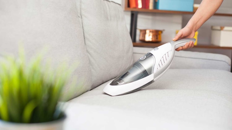 Woman using handheld vacuum cleaner to clean sofa