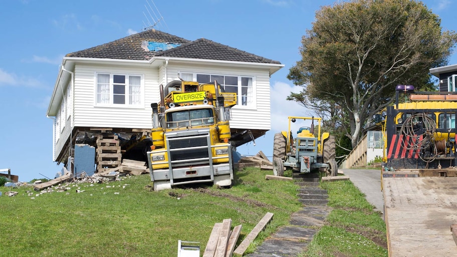 A house is removed from its location and loaded onto a truck for transportation.