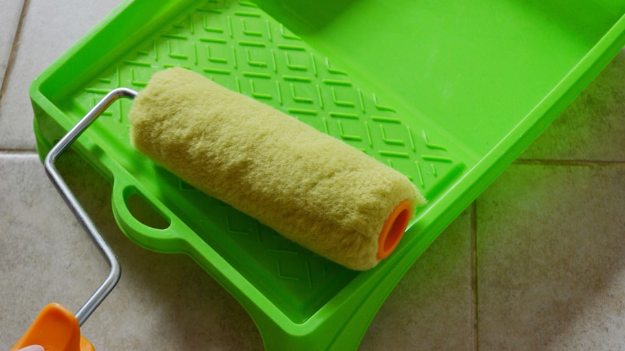 A green paint tray and paint roller on a tile floor