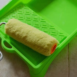 A green paint tray and paint roller on a tile floor