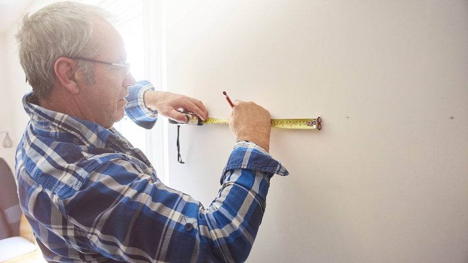 man measures the wall near his window to find the wall studs 