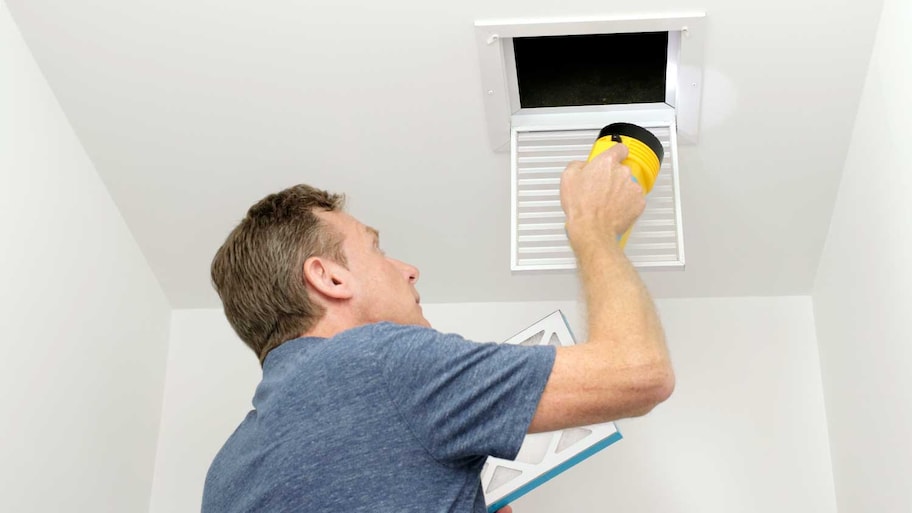 Homeowner using a flashlight to inspect an air vent