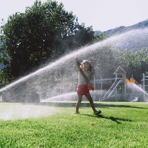 A kid playing while sprinklers are watering the lawn