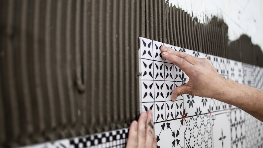 Close-up of a man’s hands applying ceramic tiles on a wall