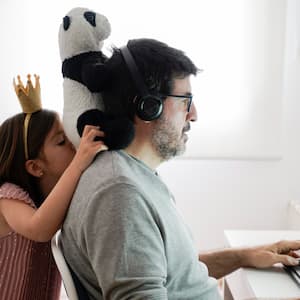 A man working on his computer with his daughter playing behind him