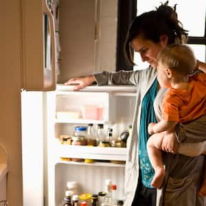 A mother holding her baby looking inside the refrigerator