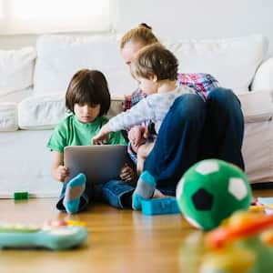 A mother with her two kinds using a tablet while sitting on laminate floor