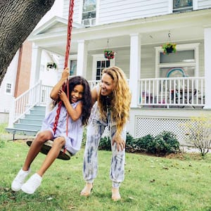 A mother pushing her daughter on a swing in their front yard