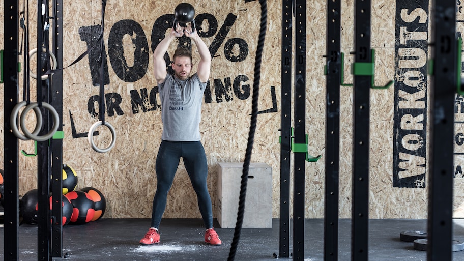 Man in gym clothes working out with a kettlebell in a garage home gym with an inspirational quote painted on the wall behind him