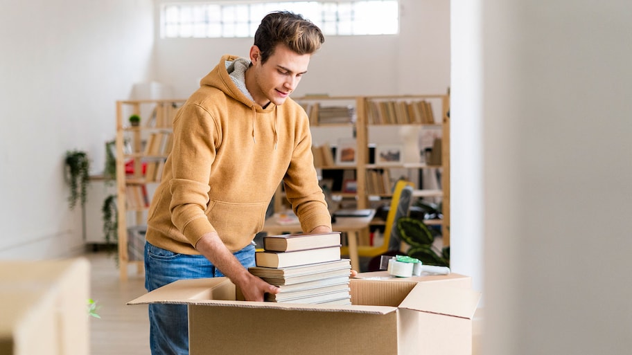 Man putting a pile of books in a cardboard box