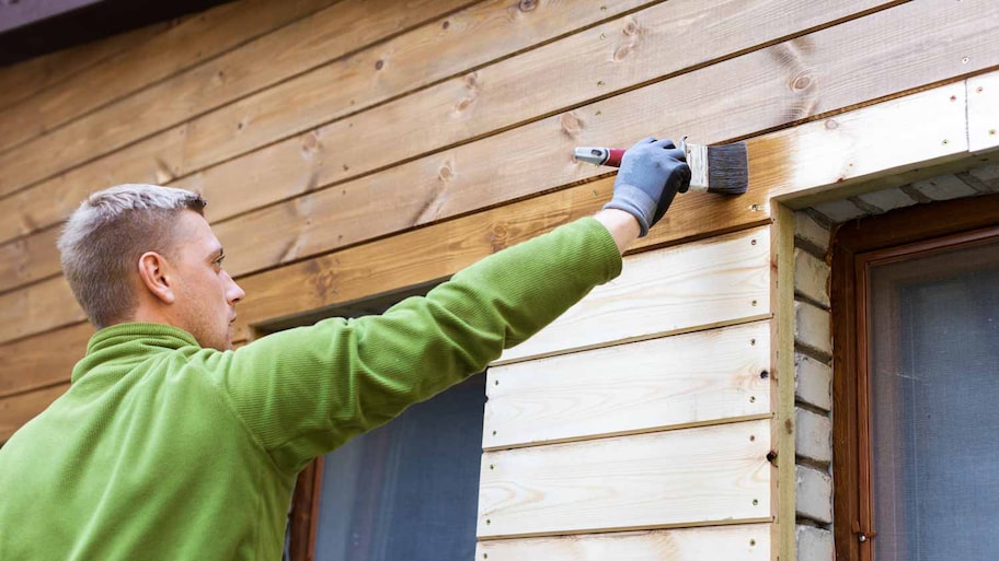 A person coating with a brush a wood siding