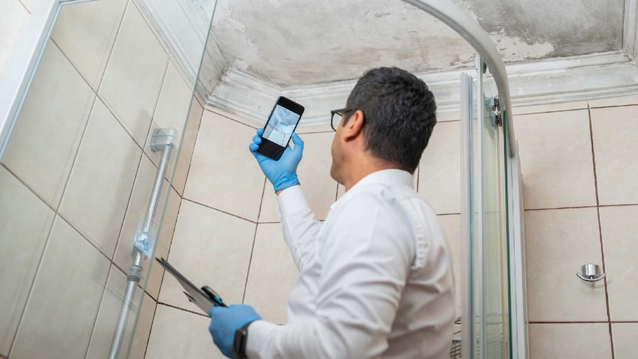 A person inspecting black mold on a ceiling