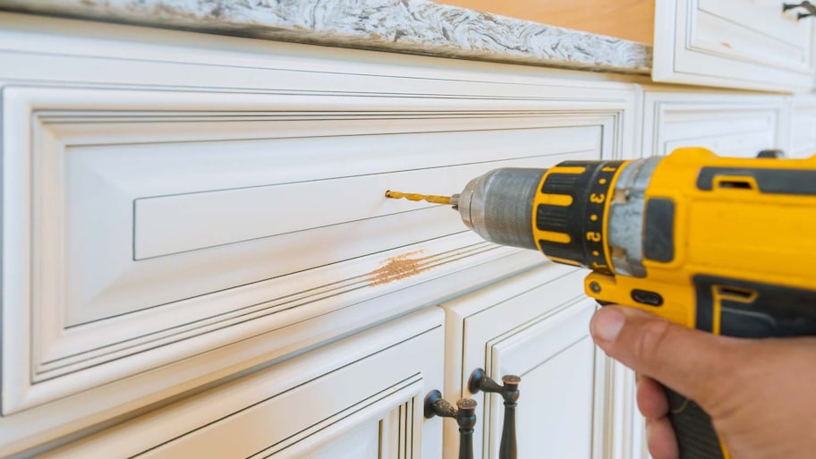 A person using a drill installing a handle in a cabinet drawer