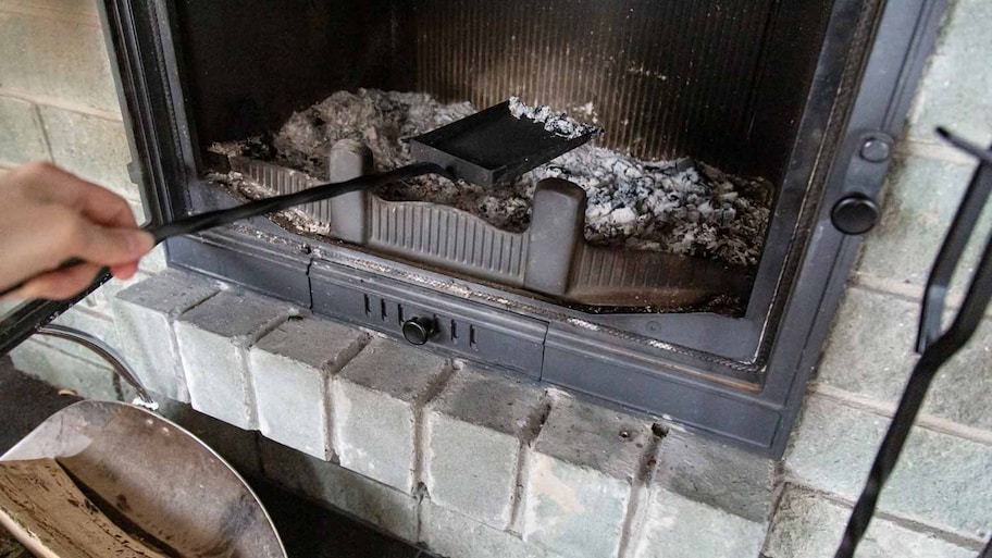 A person removing ashes from a stone fireplace