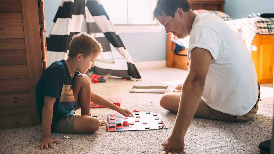 Father and son sitting on the carpet and playing checkers