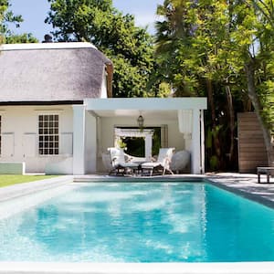 A pool in a lush backyard with some lawn chairs