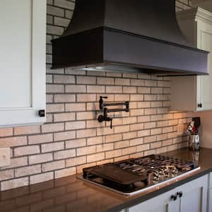 A traditional kitchen with a pot filler faucet and a large hood vent over a gas stove