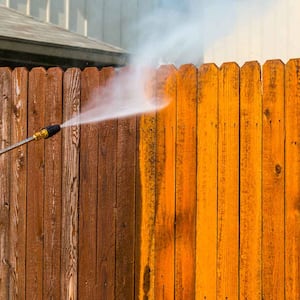 man pressure washing wooden fence