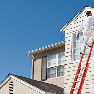 A professional standing on a ladder paints the exterior of a house