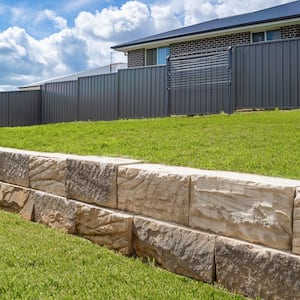 a stone retaining wall with green grass and a fence in the background