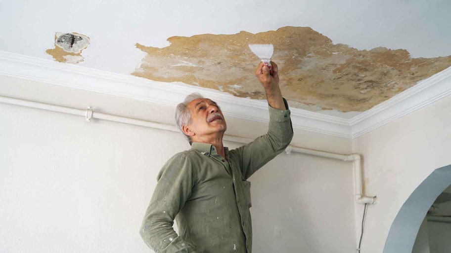 Man removing paint from water damaged ceiling