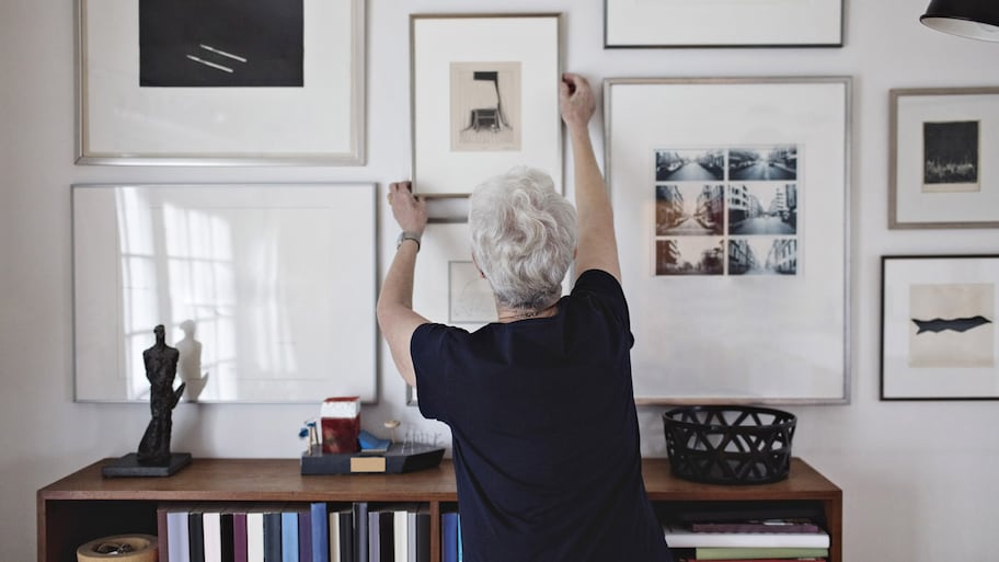 A senior woman adjusting picture frame on a wall