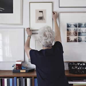 A senior woman adjusting picture frame on a wall